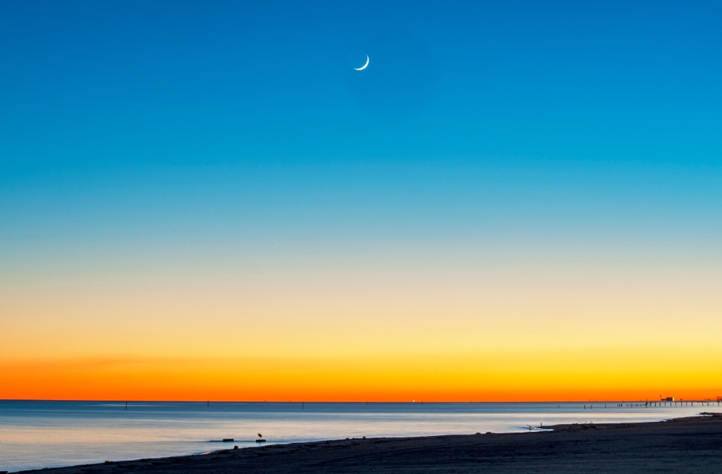 Vibrant Coastal Sunset with Crescent Moon Orange to Blue Gradient Sky and Quiet Beach Horizon.jpg