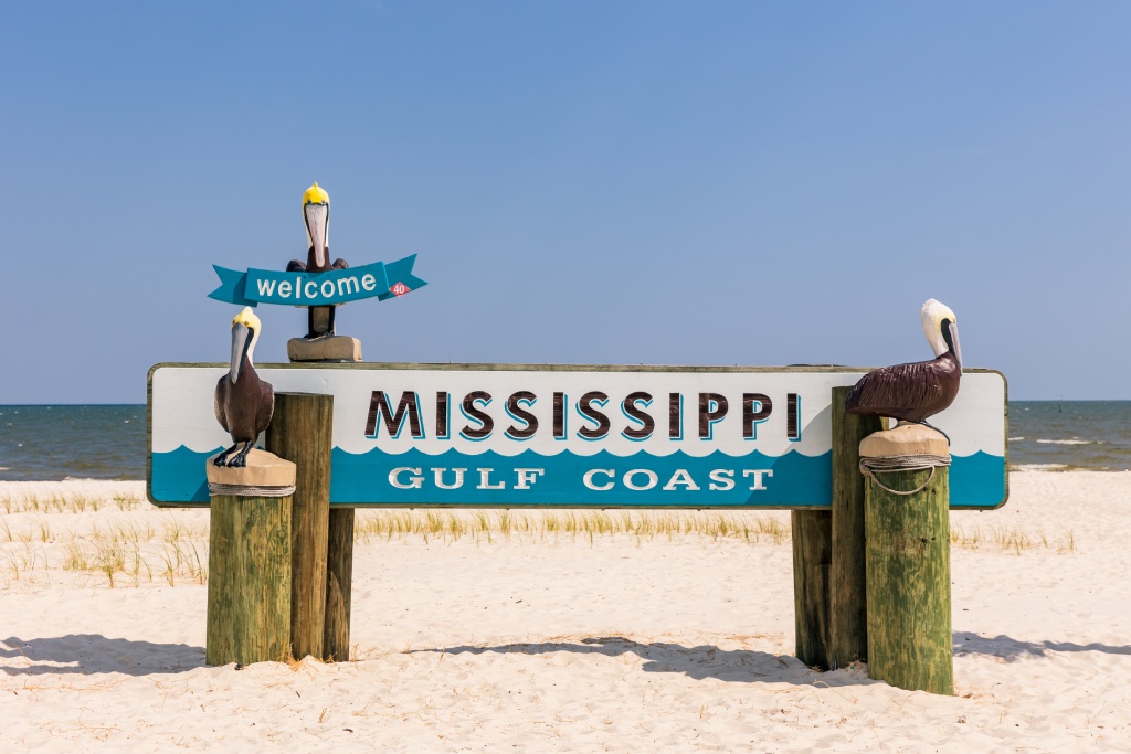 Welcome to Mississippi Gulf Coast Beach Sign with Pelican Statues and Ocean Background